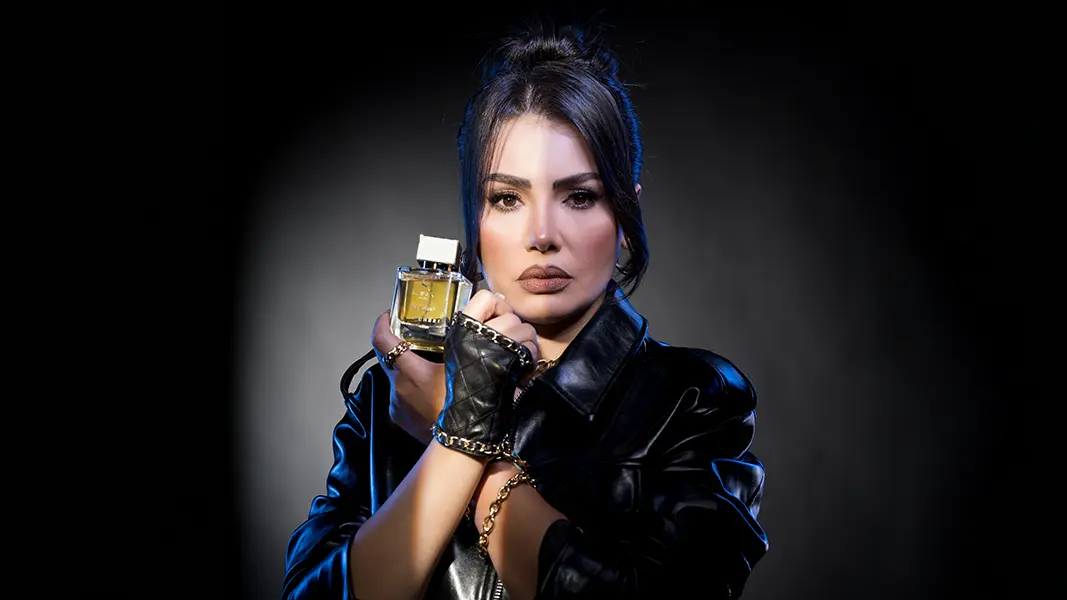 Studio portrait of a model holding a perfume bottle under a single hard light